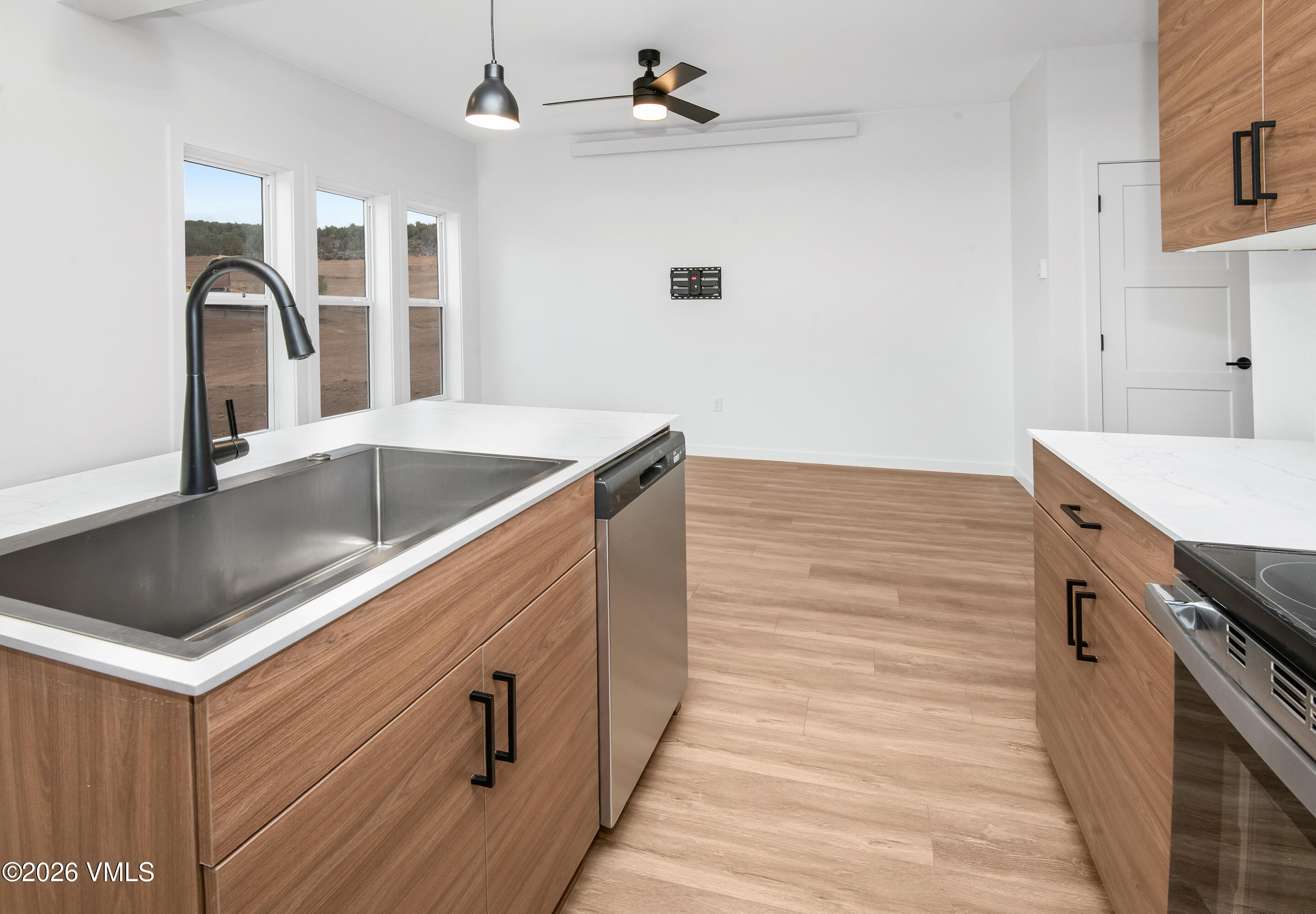 Vacant kitchen with wood-grain cabinets, white countertops, and a large stainless-steel sink.