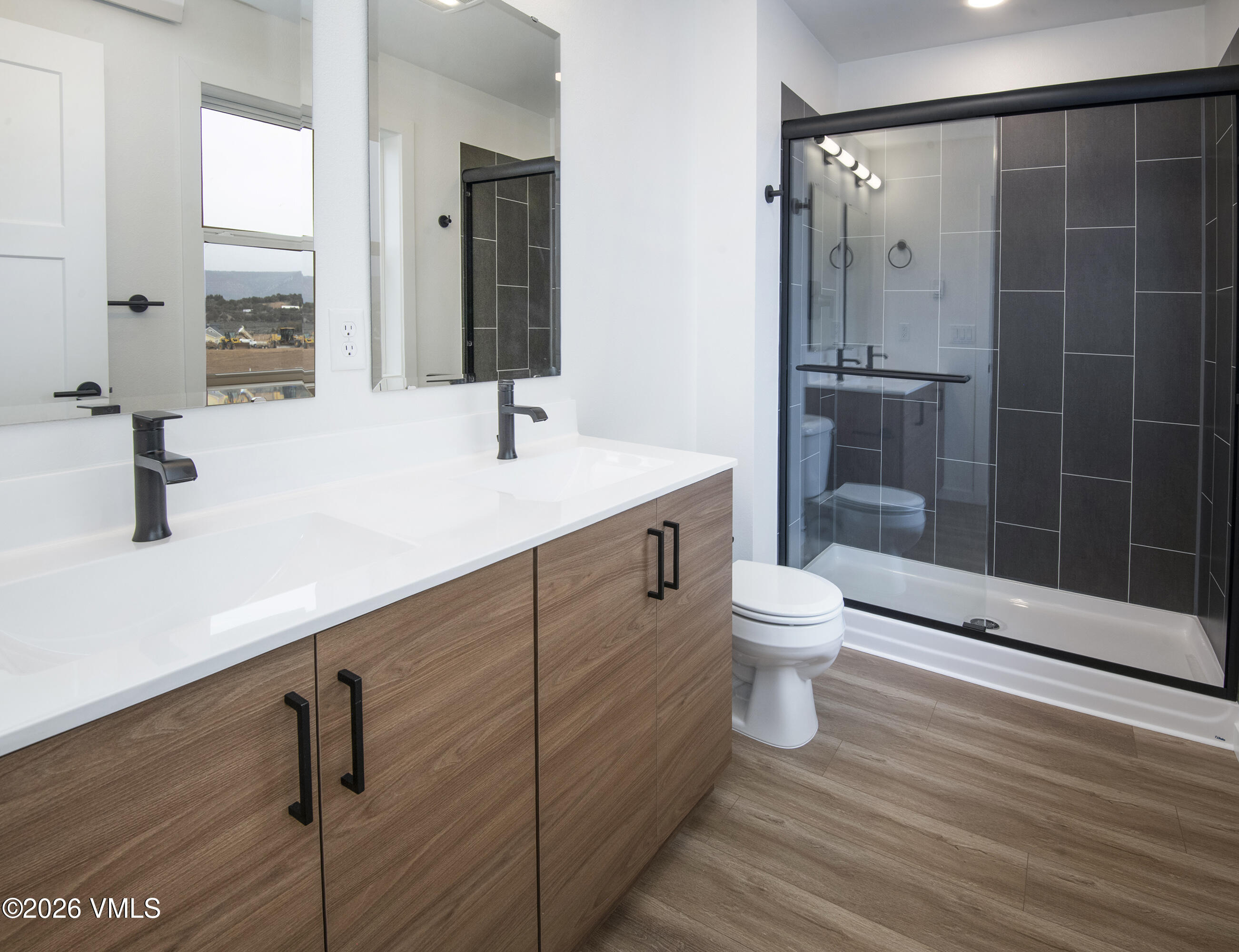 Bathroom with a double-sink wood vanity and glass shower lined with dark tile.