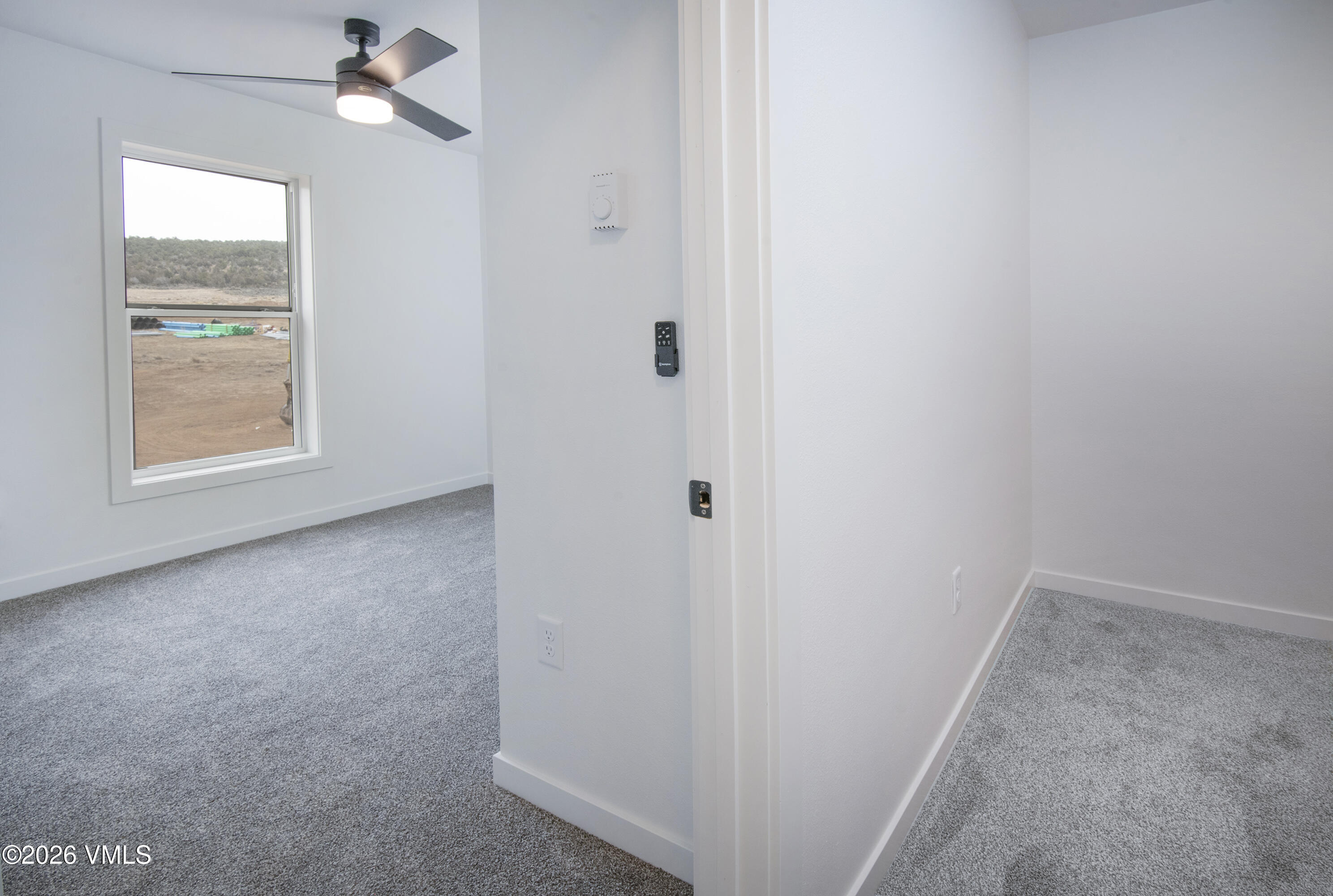 Empty carpeted bedroom with a ceiling fan and large window overlooking a dry hillside.