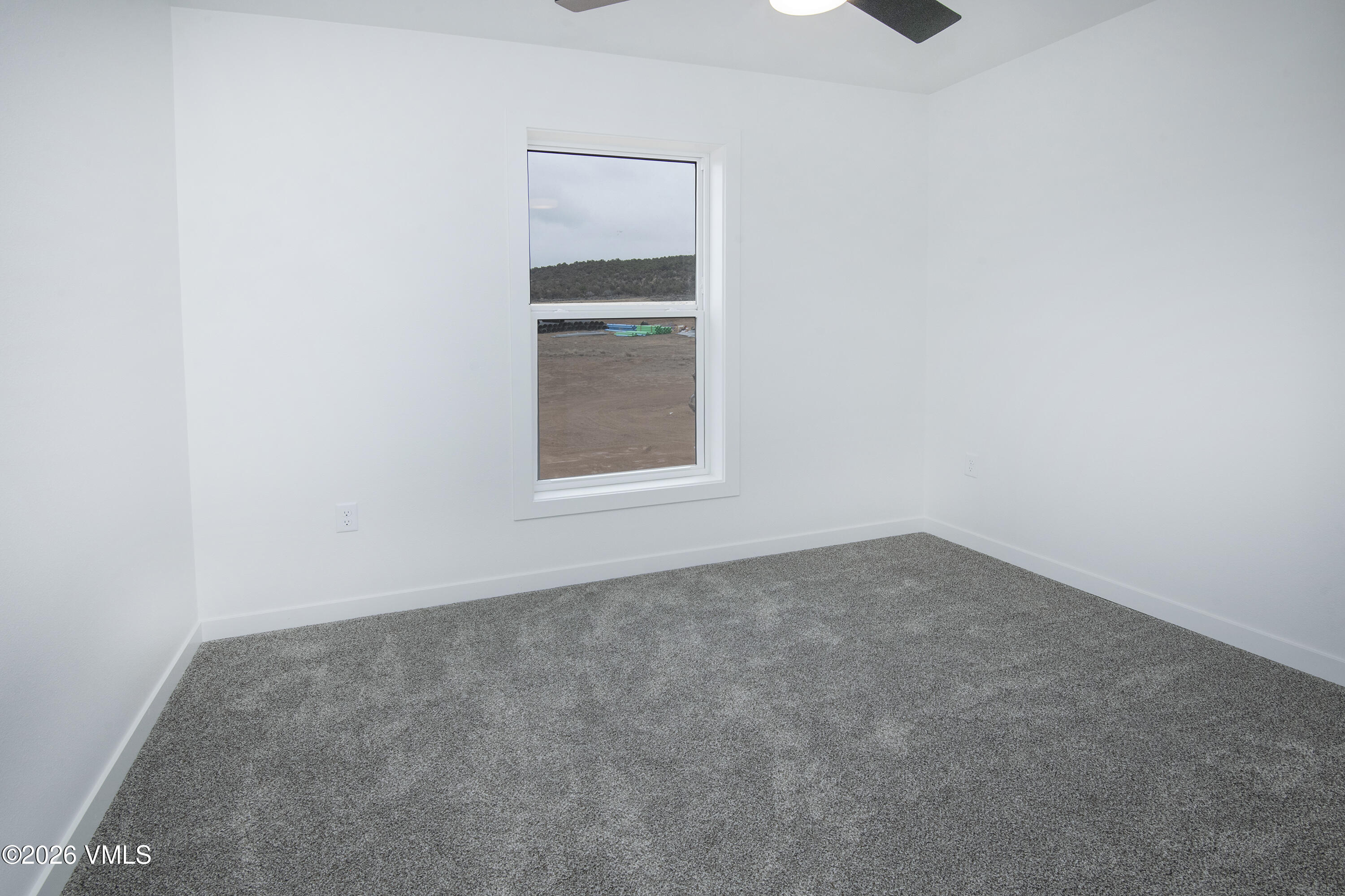 Empty room with gray carpet, a window overlooking graded ground, and a ceiling fan.