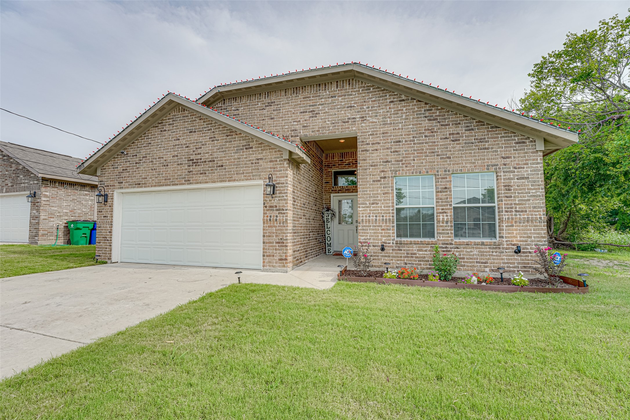Brick house with a two-car garage, covered entry, and colorful flower bed.