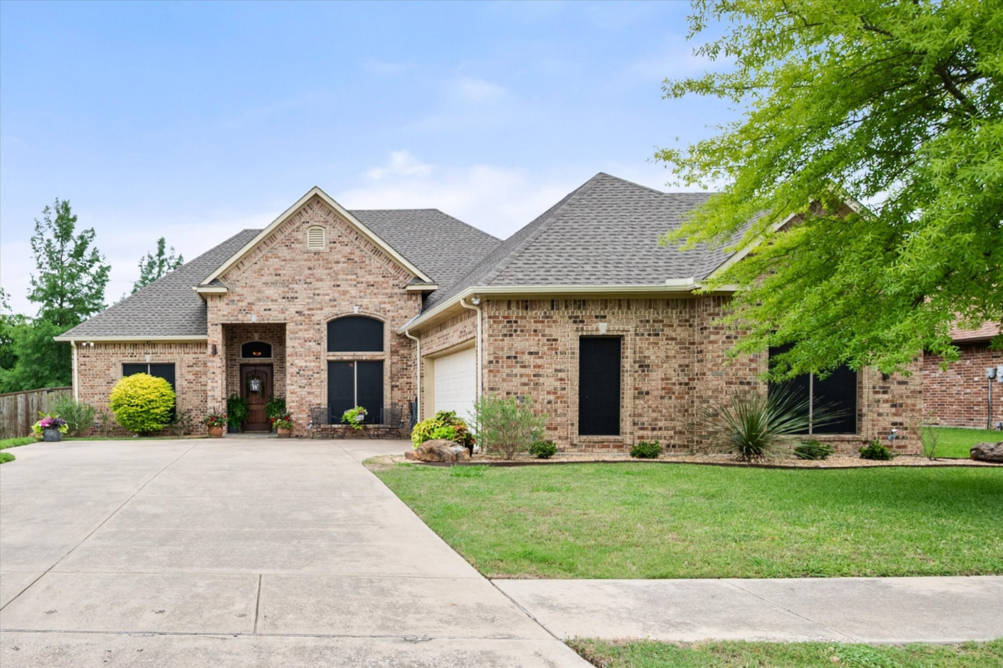 Brick house with a gray shingle roof, landscaped lawn, and wide concrete driveway.