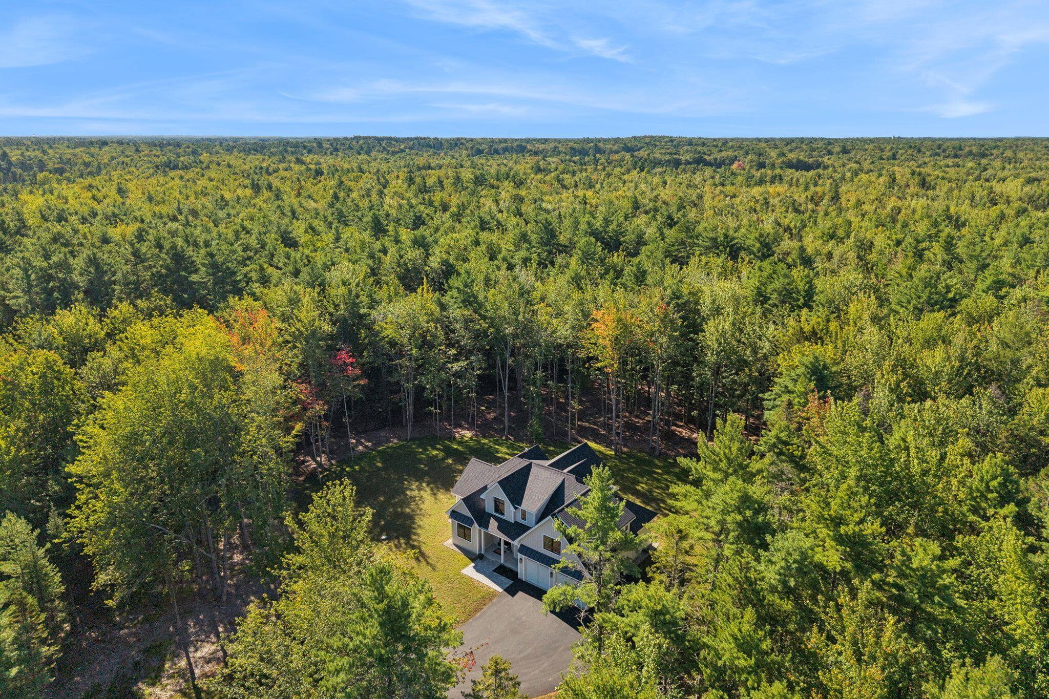 Aerial view of a house surrounded by dense woodland, with a driveway and lawn.