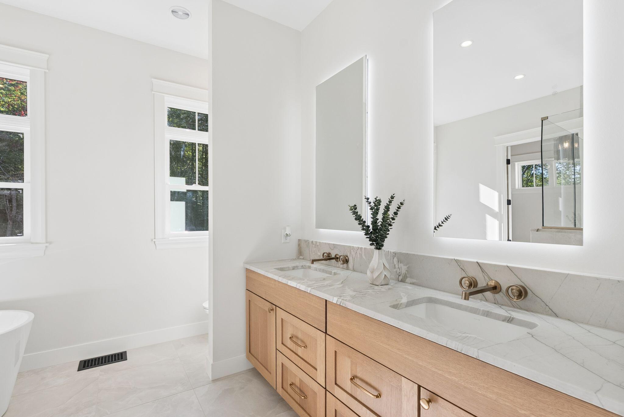 Bright bathroom with a double-sink marble vanity, light wood cabinetry, and a glass-enclosed shower.