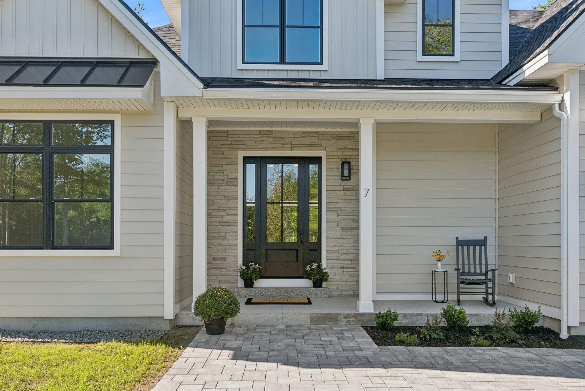 House entrance with a stone accent wall, black glass-paneled door, and covered porch.