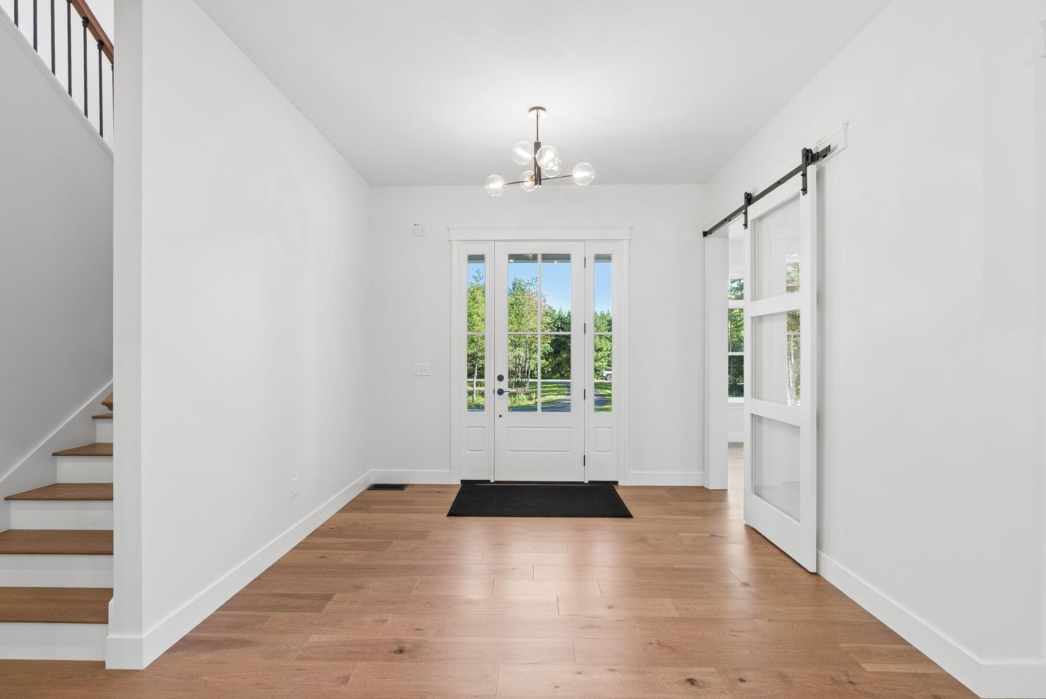 Entry foyer with wood floors, a glass-paneled front door, staircase, and sliding barn door.