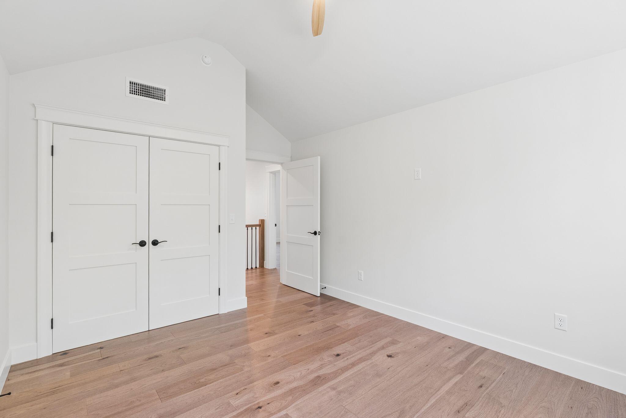 Vacant room with vaulted ceiling, wood floors, and double closet doors.