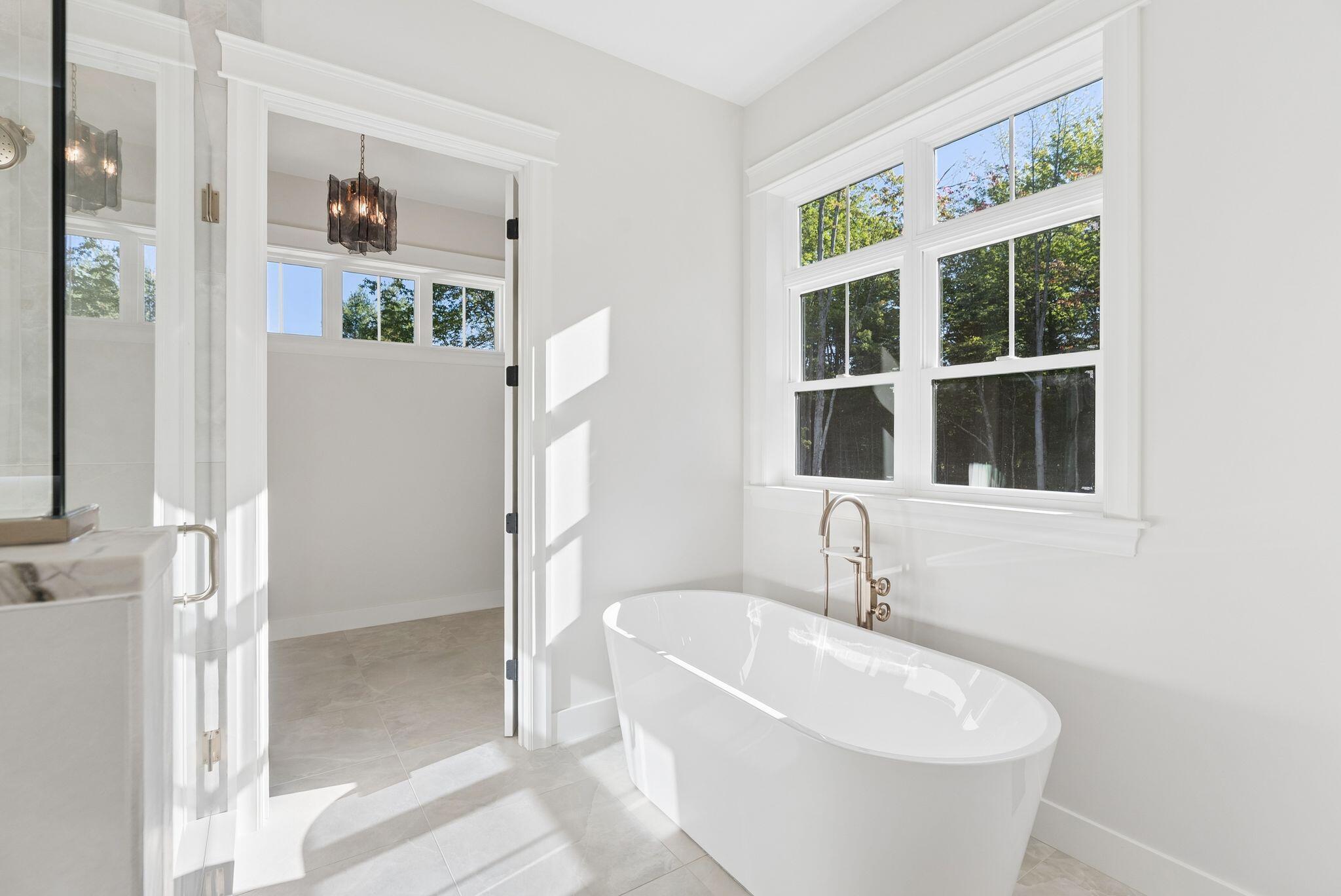 Bright bathroom with a freestanding tub beneath large windows overlooking trees.