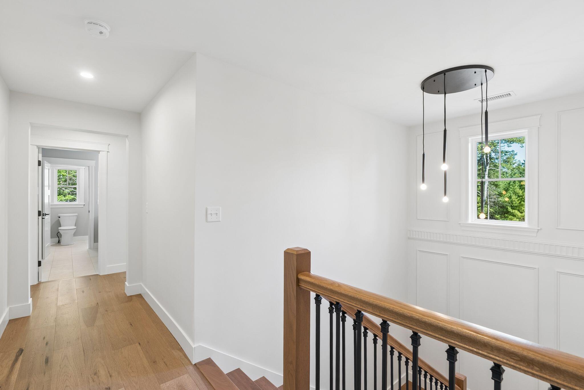 Bright upstairs landing with oak floors, a black-and-wood stair railing, and a pendant light beside a bathroom doorway.