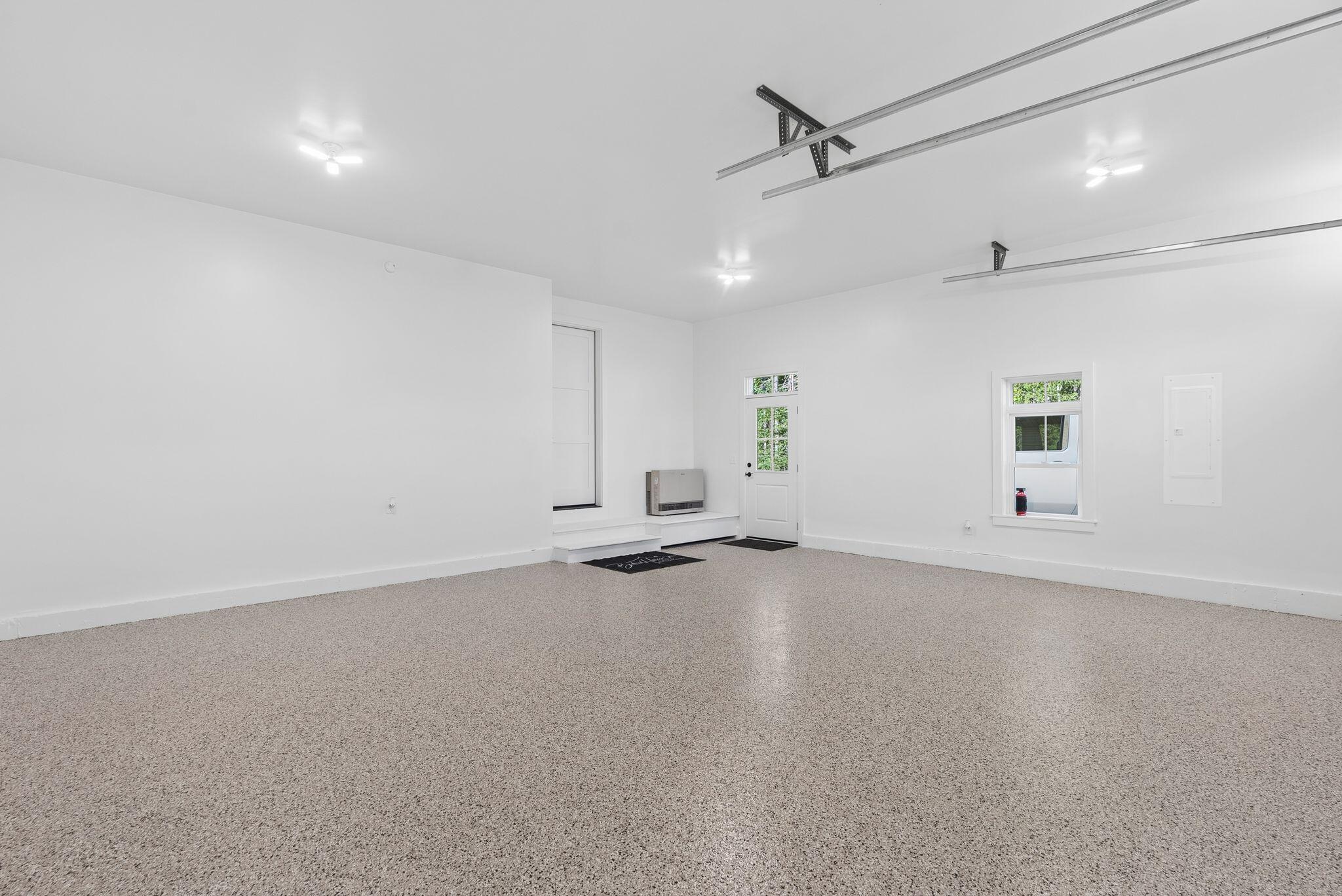 Vacant garage with carpeted floor, overhead door tracks, windows, and an exterior door.