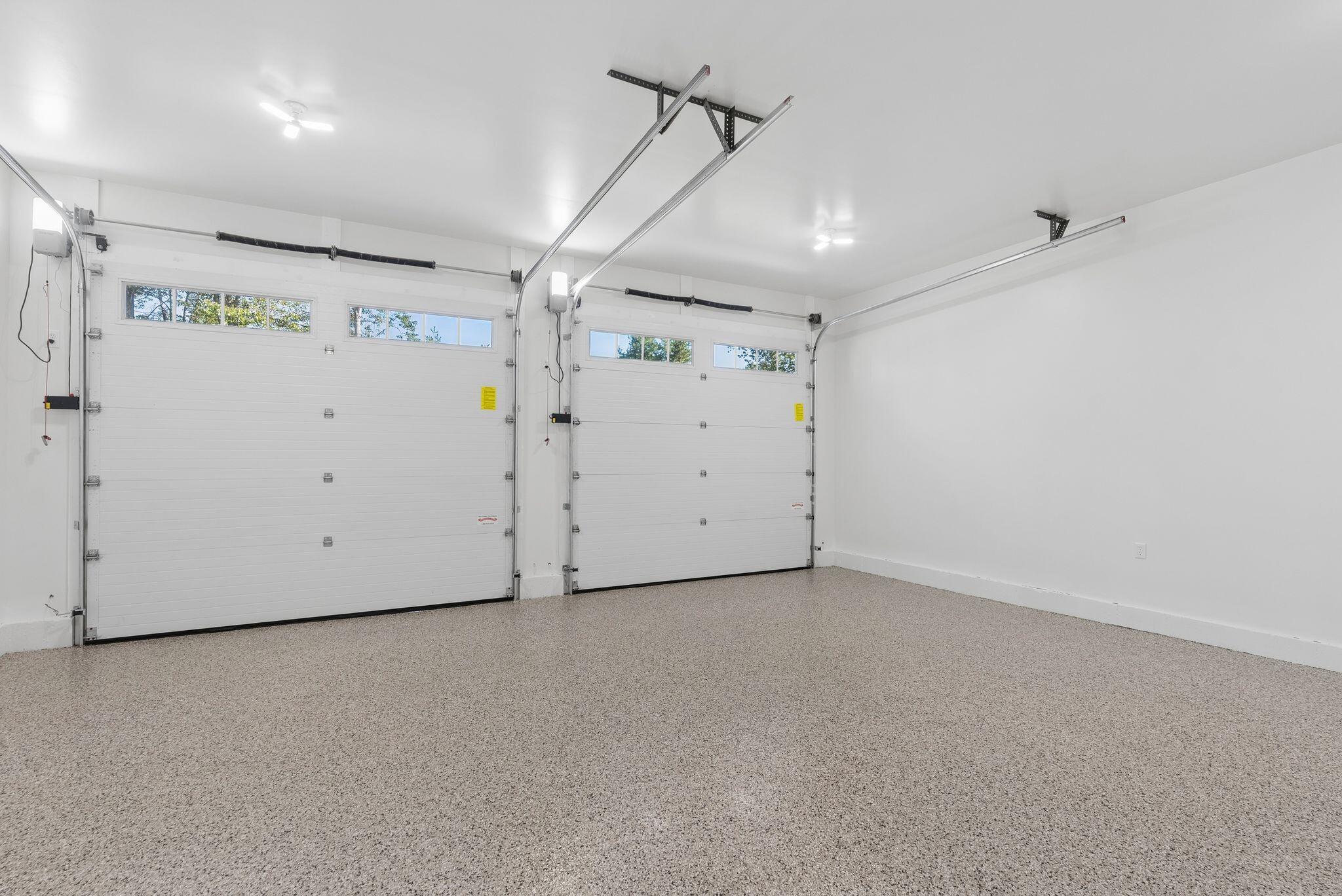 Empty two-car garage with two white overhead doors and a speckled floor.