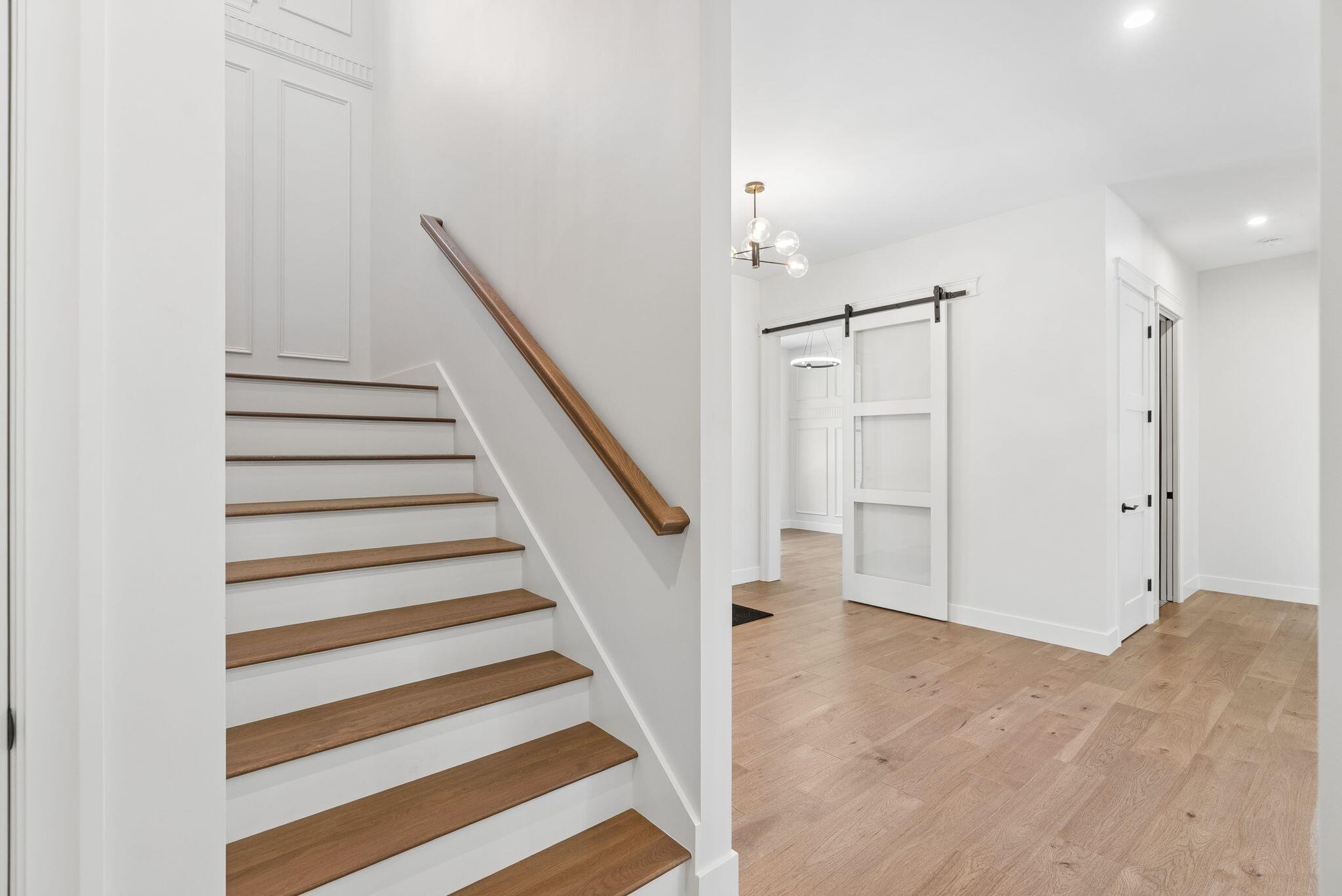 Interior staircase with wood treads and handrail beside an oak-floored hall and glass-paneled barn door.