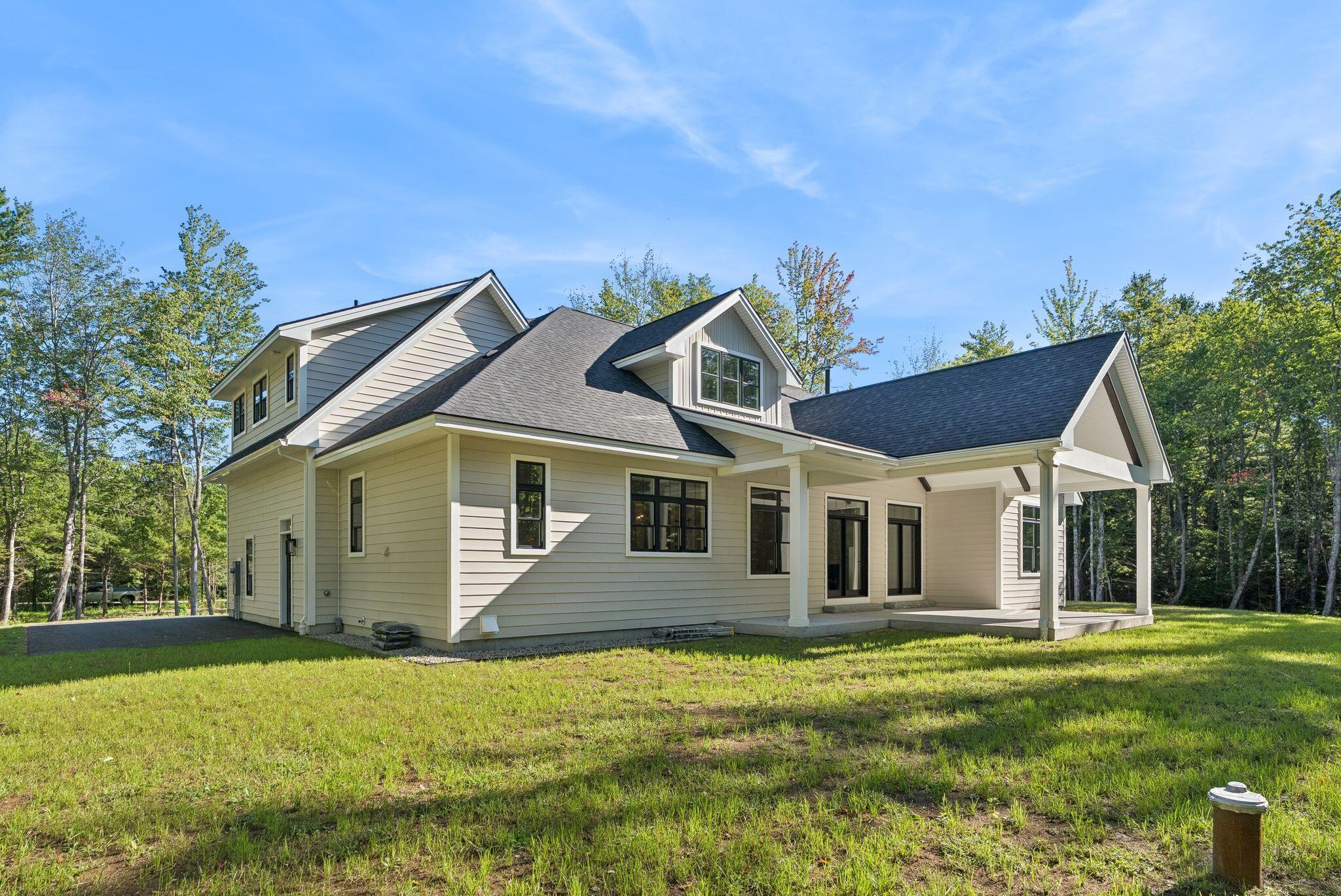 Light-colored house with a covered porch and multiple gables, set among trees beside a grassy yard.