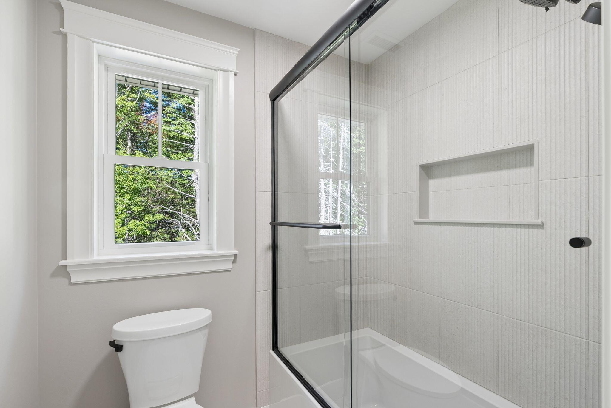 Bathroom with glass-enclosed tub and shower, recessed wall shelf, and window overlooking trees.