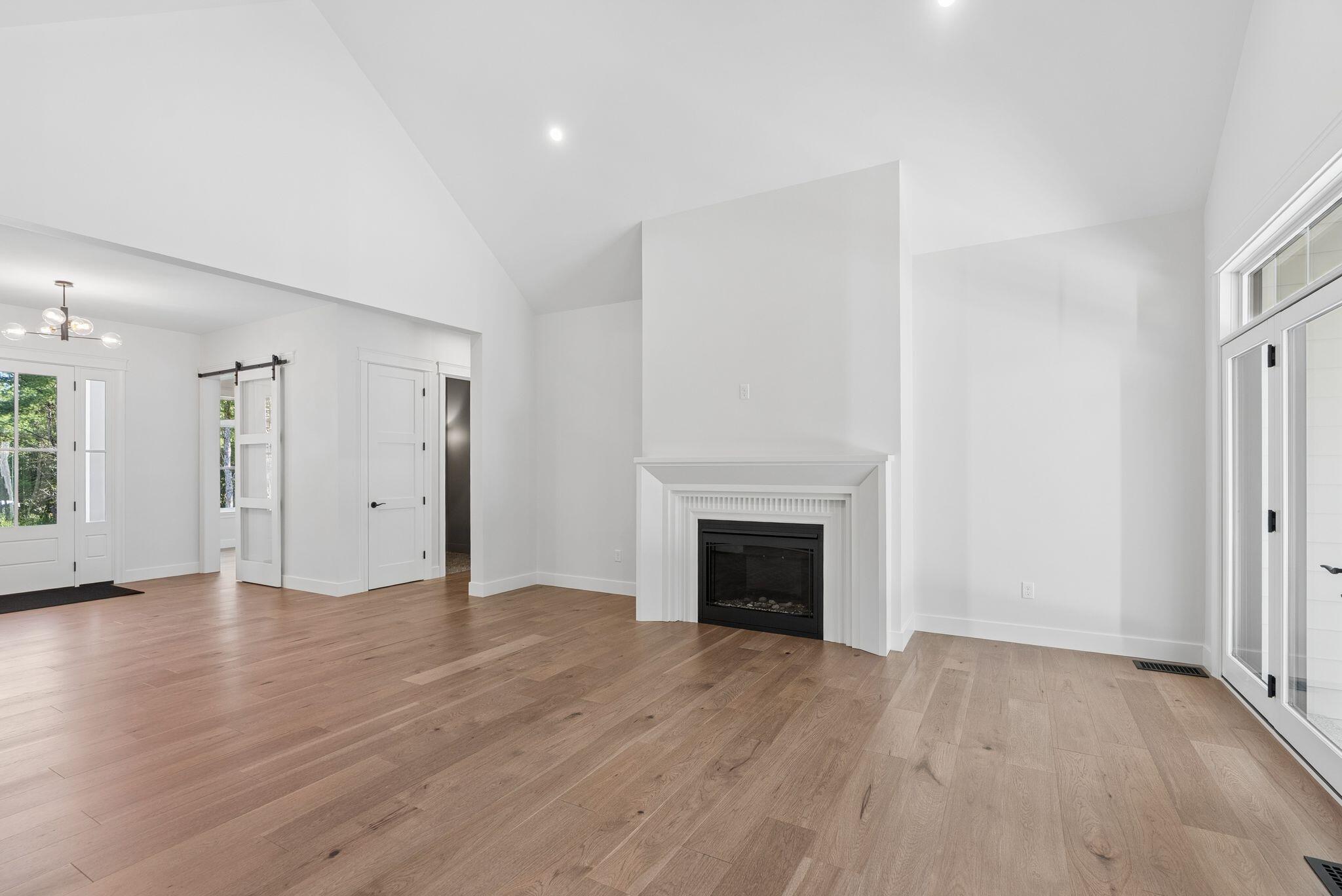 Living room with vaulted ceiling, wood floors, white fireplace, and glass doors.