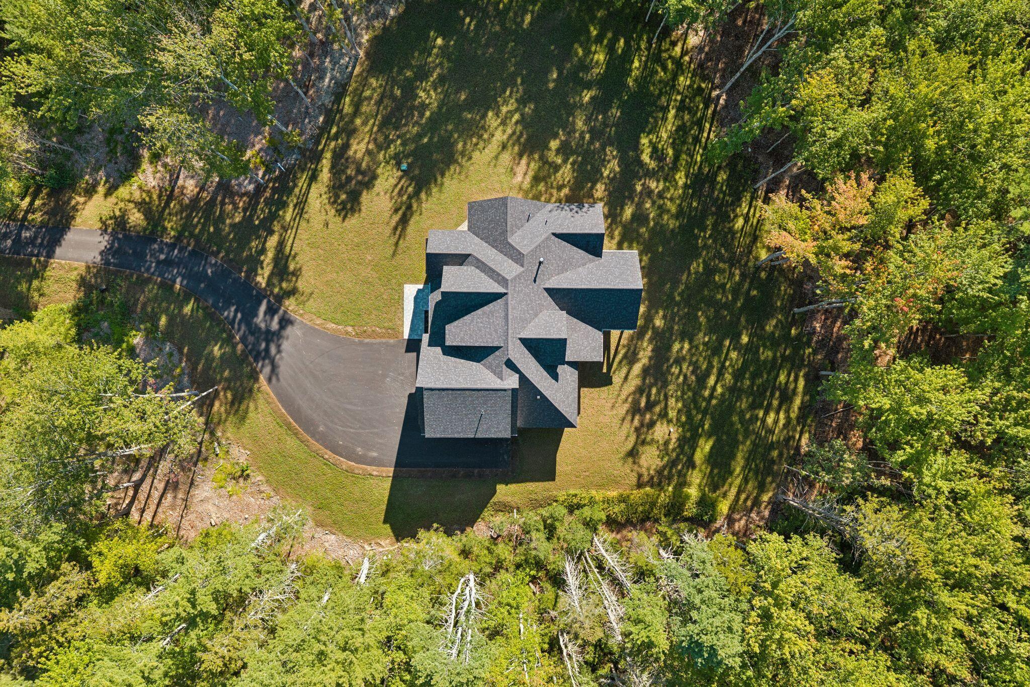 Aerial view of a house and curved driveway amid a wooded lot.