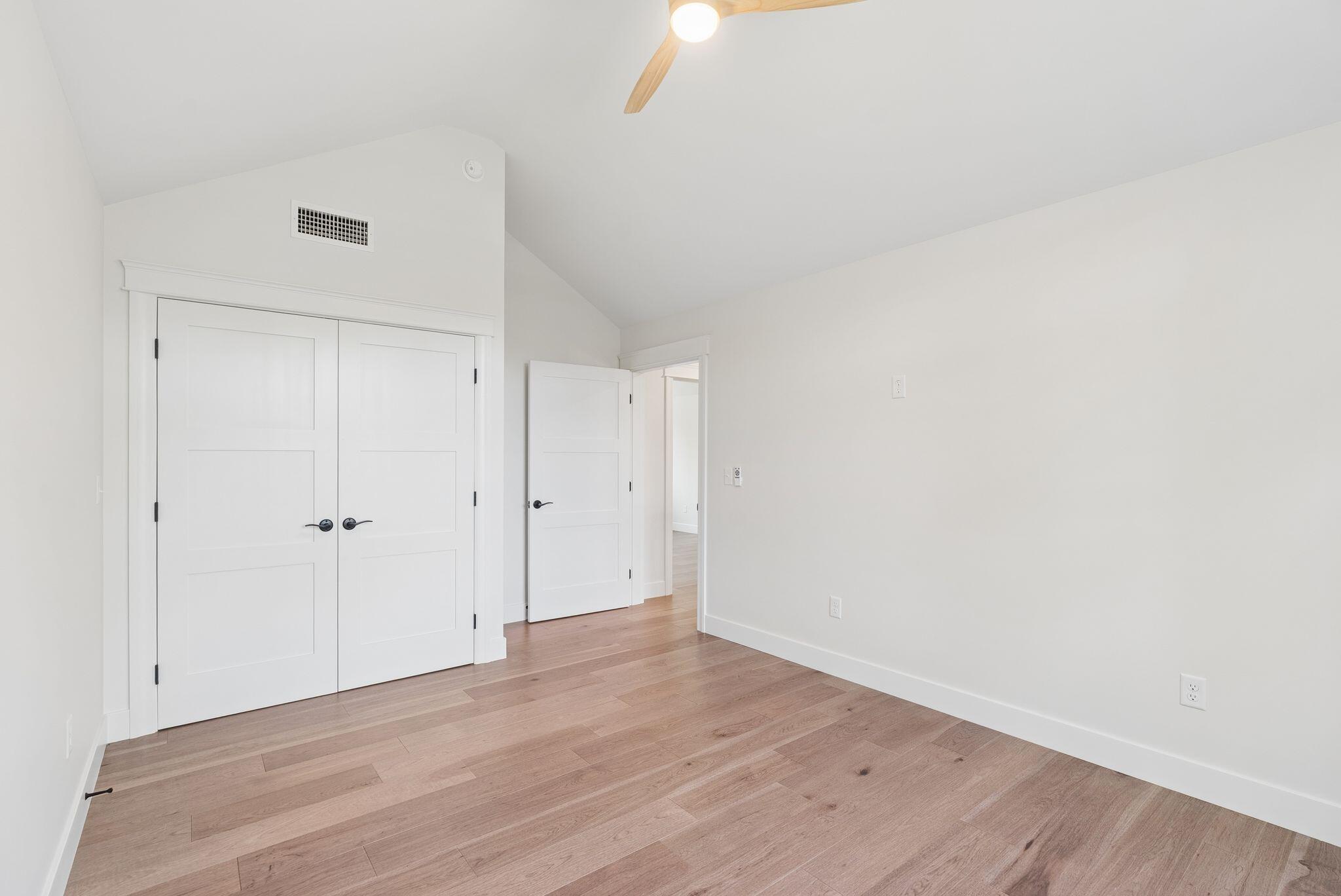 Empty room with light wood floors, a high sloped ceiling, and double closet doors.