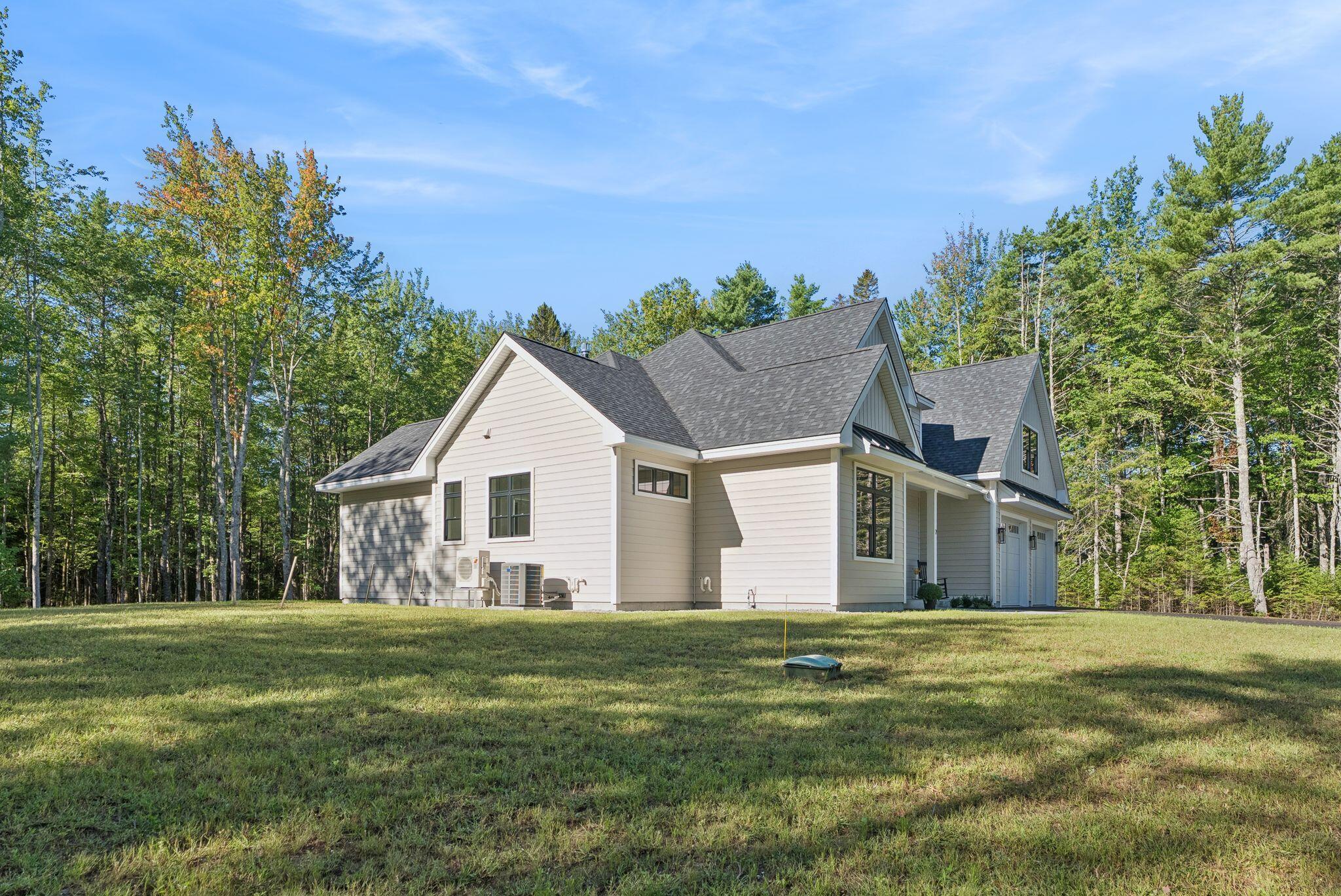 Rear and side of a light-colored home with multiple gables, a dark roof, and a wooded lawn.