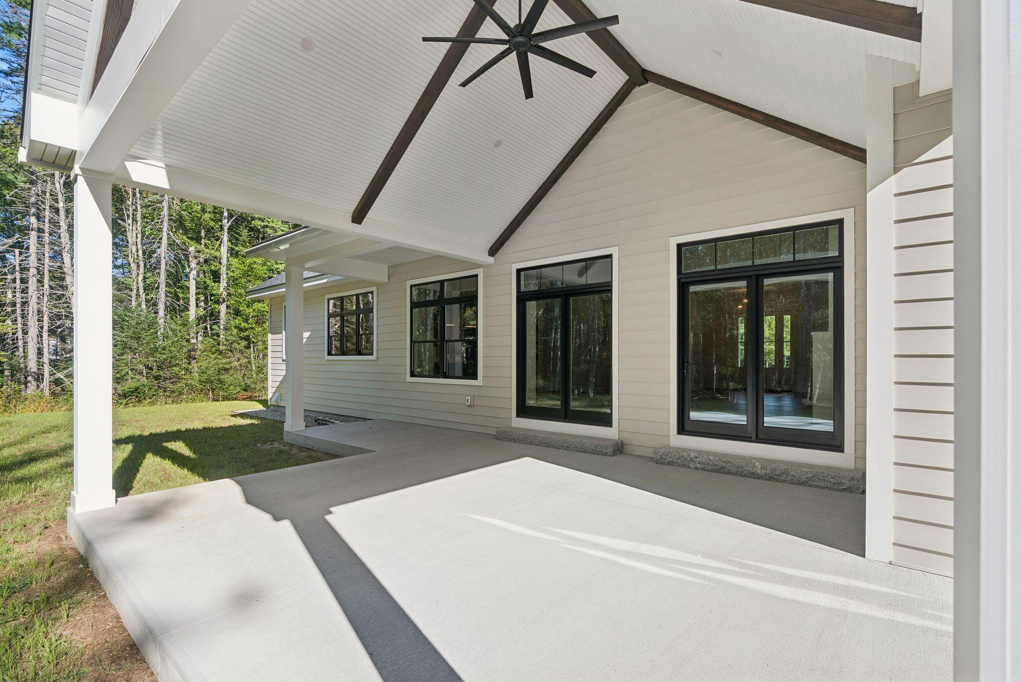 Covered patio with a high ceiling, dark beams, ceiling fan, and black-framed glass doors.