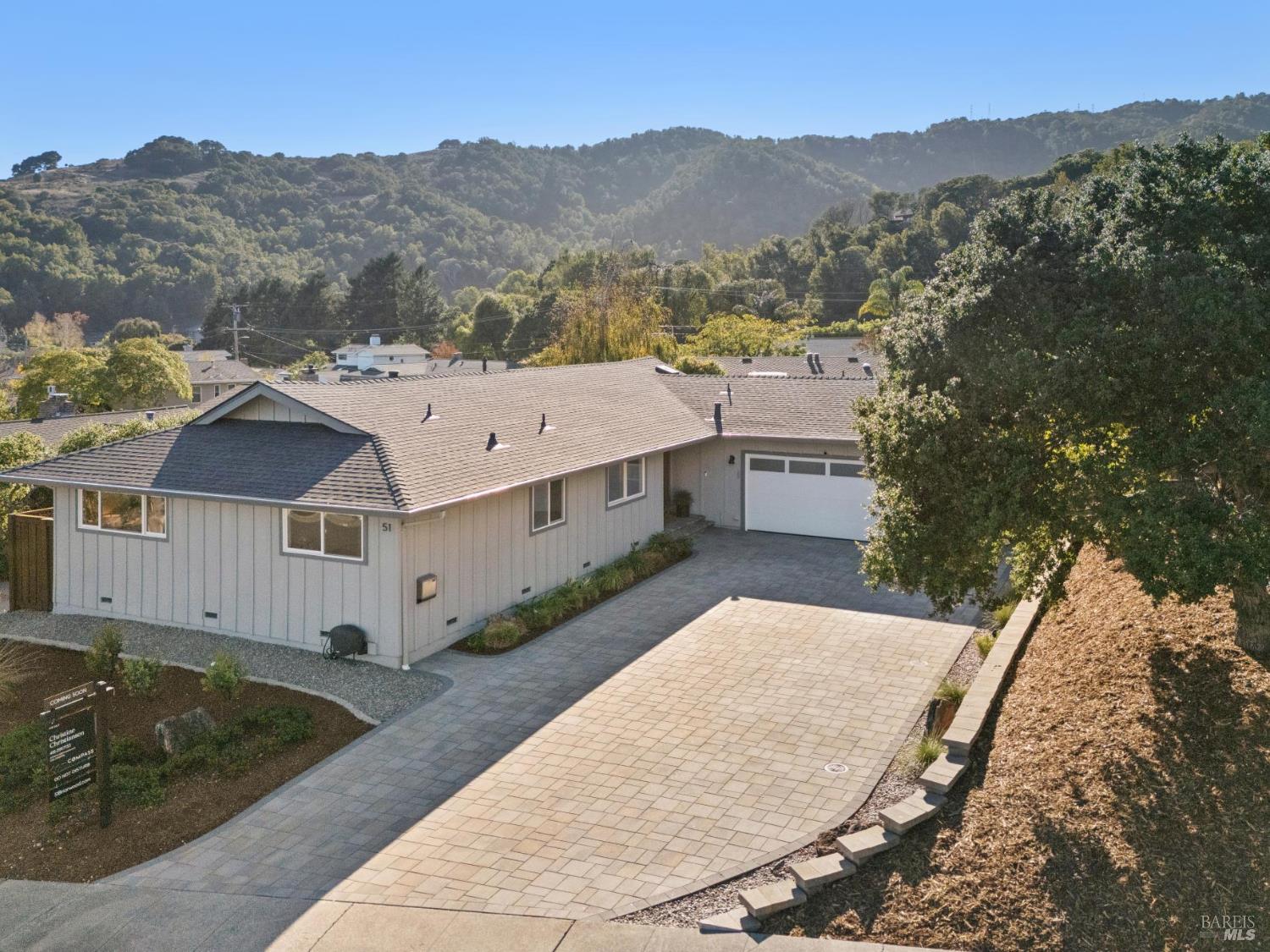Single-story home with a broad paved driveway and garage, backed by wooded hills.