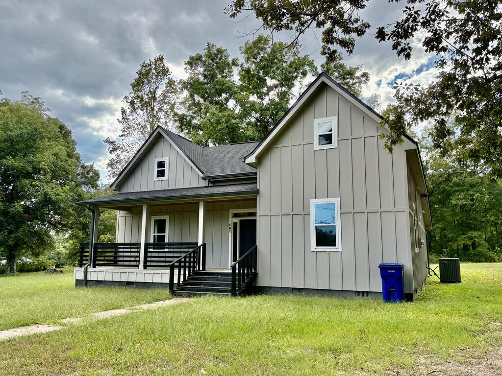 Light gray house with two front gables, a covered porch, black railings, and a broad grassy yard.