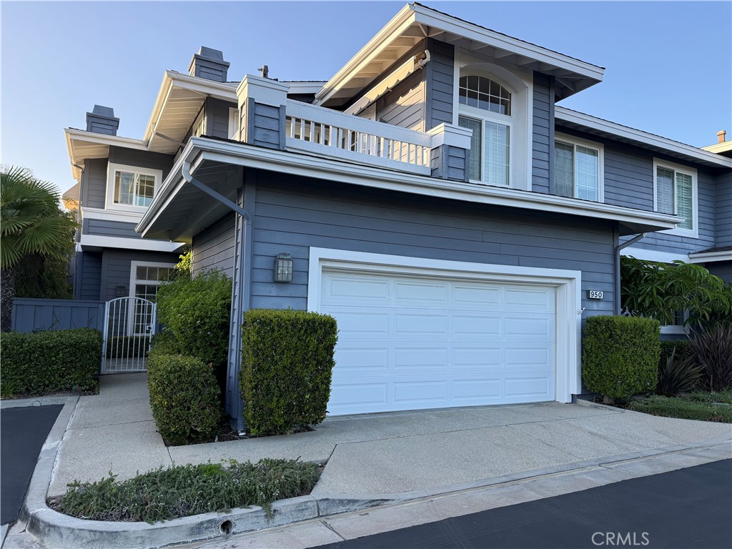 Two-story blue house with a white double garage door, upper balcony, and trimmed shrubs.
