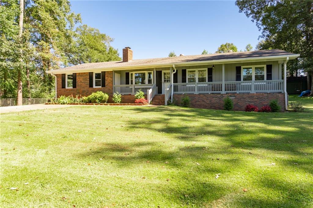 Single-story brick house with a long covered porch and broad green lawn.