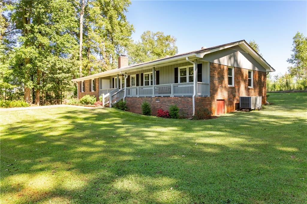 Single-story brick home with a long covered porch, broad lawn, and mature trees.