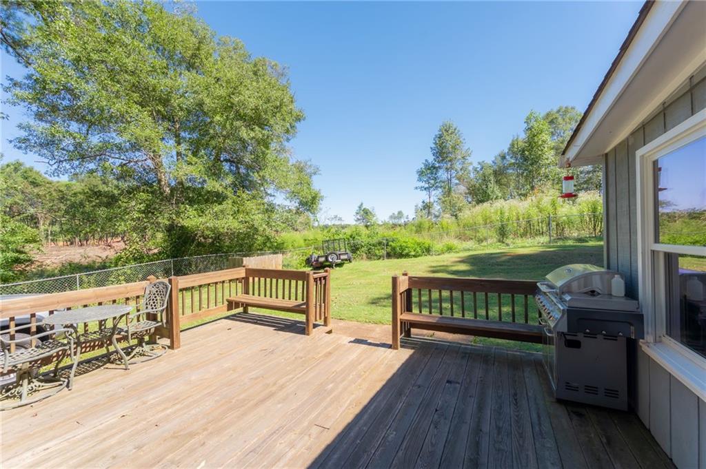Wooden deck with an outdoor dining set and grill overlooking a fenced, tree-lined yard.
