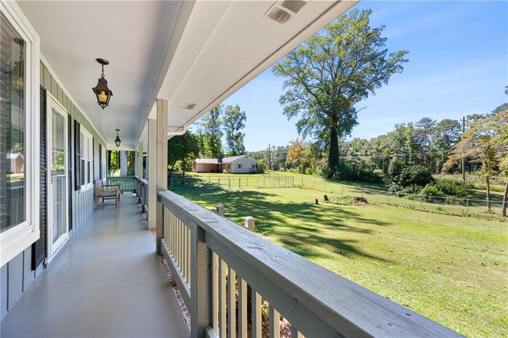 Covered porch overlooking a fenced lawn, mature trees, and a small outbuilding.