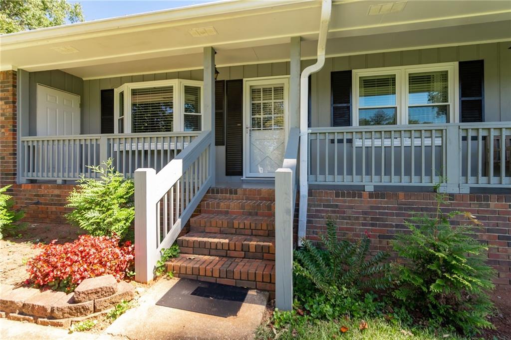 Home entrance with a covered porch, gray railings, brick steps, and landscaped beds.