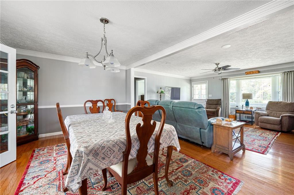 Dining and living area with hardwood floors, patterned rugs, and a teal sofa.