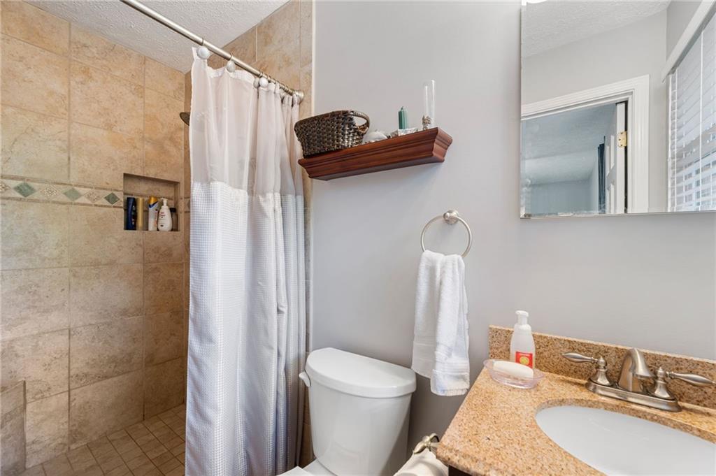 Bathroom with a tan tiled shower and granite vanity beside the toilet.
