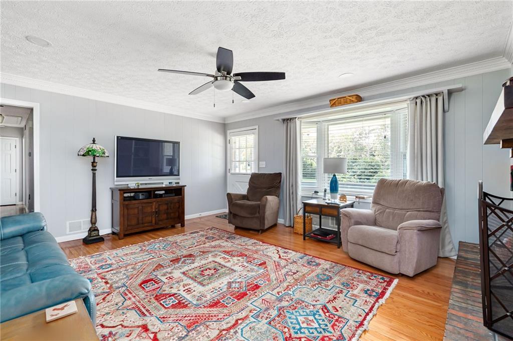 Living room with a colorful patterned rug, teal sofa, beige recliners, and a wide curtained window.