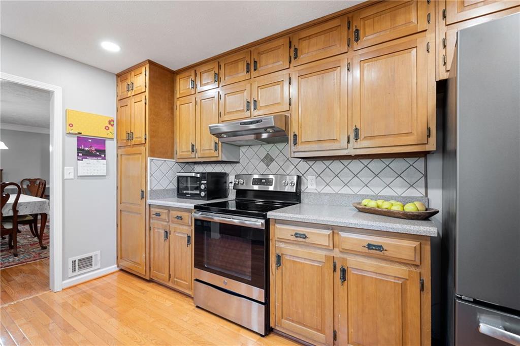 Kitchen with honey-colored wood cabinets, stainless appliances, and a diamond-pattern tile backsplash.