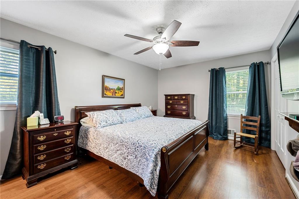Furnished bedroom with a dark wood bed, patterned bedding, hardwood floors, and teal curtains.