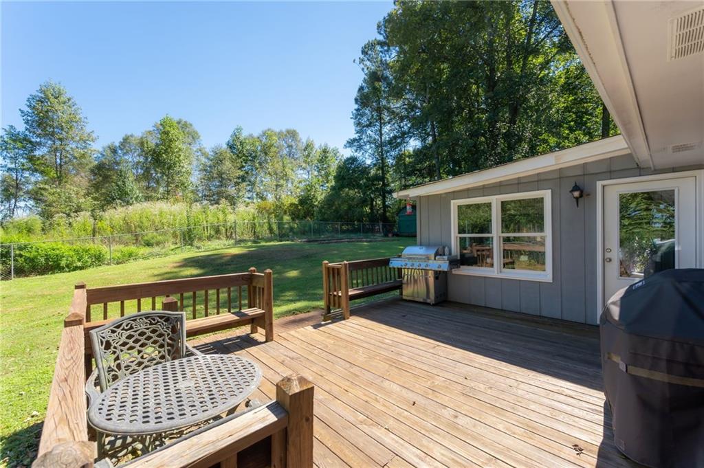 Wooden backyard deck with patio seating and grill overlooking a fenced, tree-lined lawn.