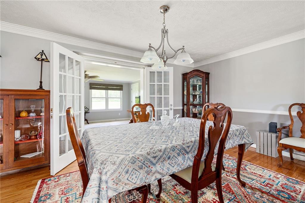 Dining room with a patterned tablecloth, carved wooden chairs, china cabinets, and French doors to a bright adjoining room.