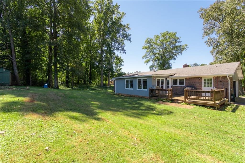 Single-story home with gray siding, brick, two wooden decks, and a wide lawn beneath mature trees.