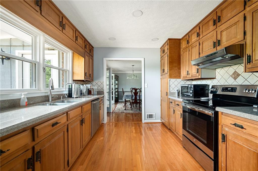 Kitchen with warm wood cabinetry, hardwood floors, stainless steel appliances, and large windows.