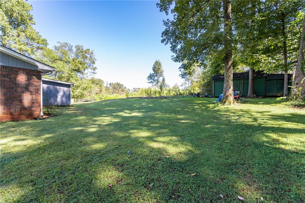 Grassy backyard with mature trees, a brick house, and green outbuildings.