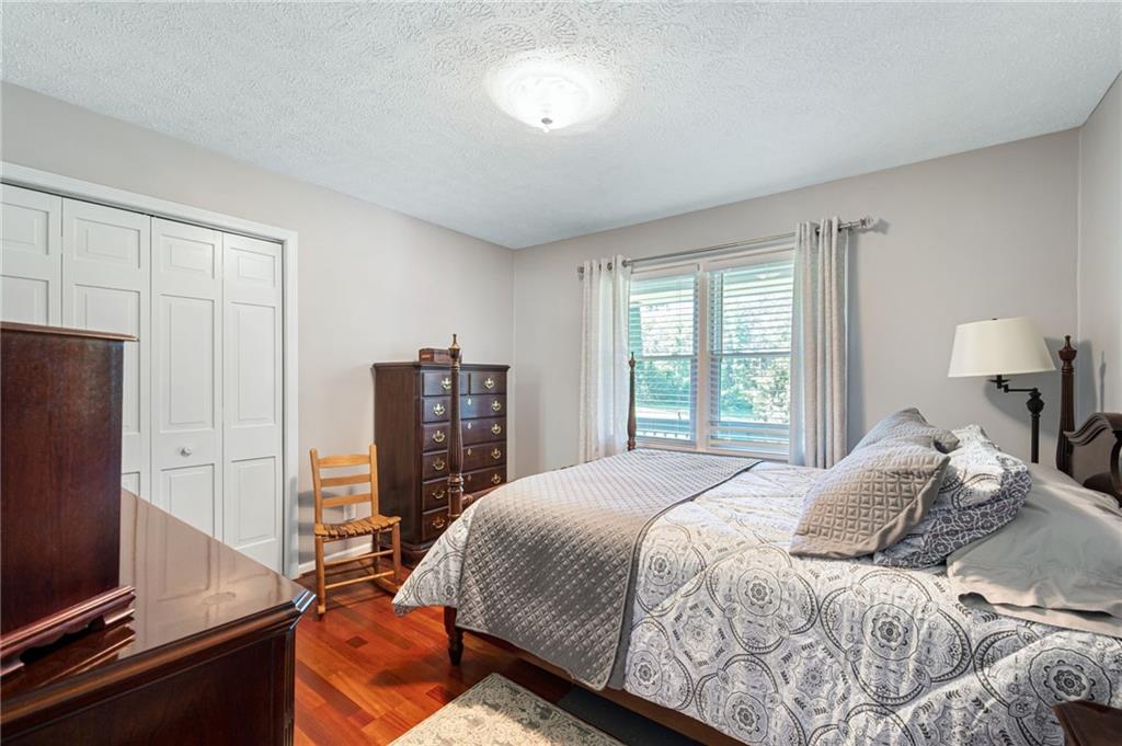 Furnished bedroom with patterned bedding, hardwood floors, and a sunlit window.