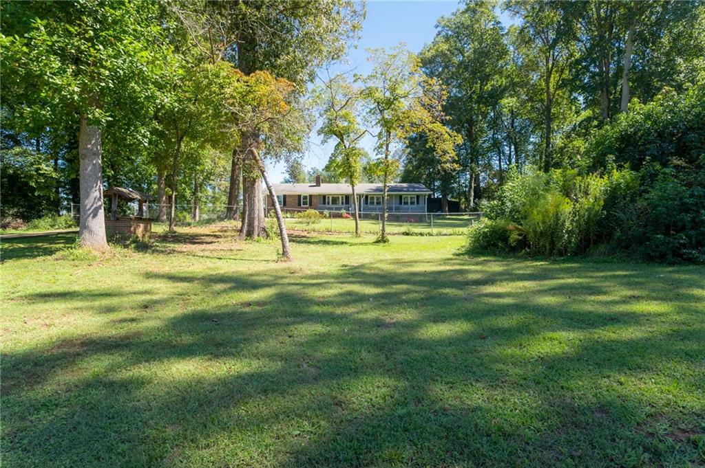 Single-story home beyond a broad grassy yard shaded by mature trees.