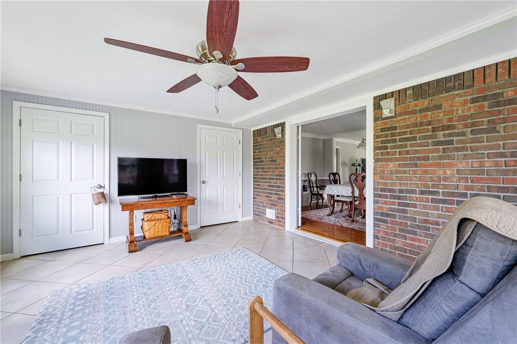 Living room with a brick accent wall, gray sofa, tiled floor, and adjoining dining room.