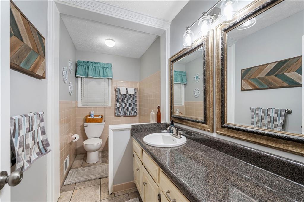 Bathroom with a long granite vanity, framed mirrors, and a toilet beneath a window with a teal valance.