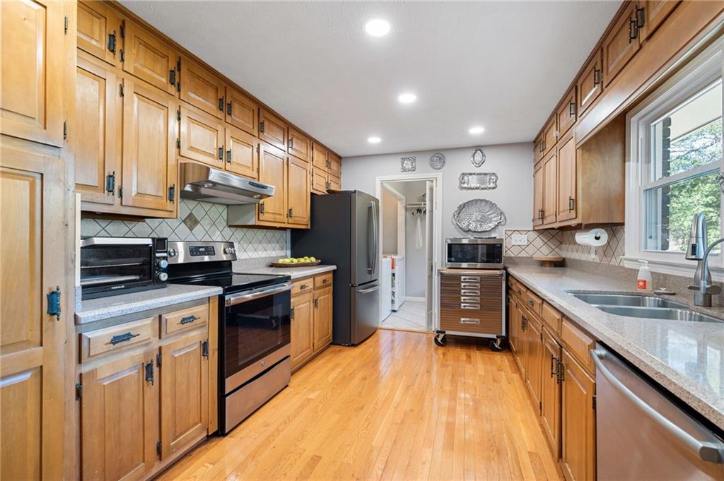 Kitchen with honey-toned wood cabinets, stainless steel appliances, and a large window above the sink.