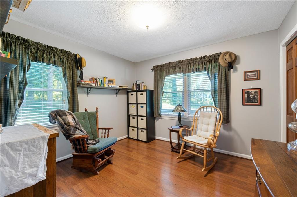 Furnished office with hardwood floors, curtained windows, a book shelf, and two rocking chairs.