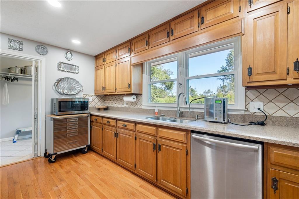 Kitchen with honey-toned wood cabinets, a window over the sink, and stainless-steel dishwasher.