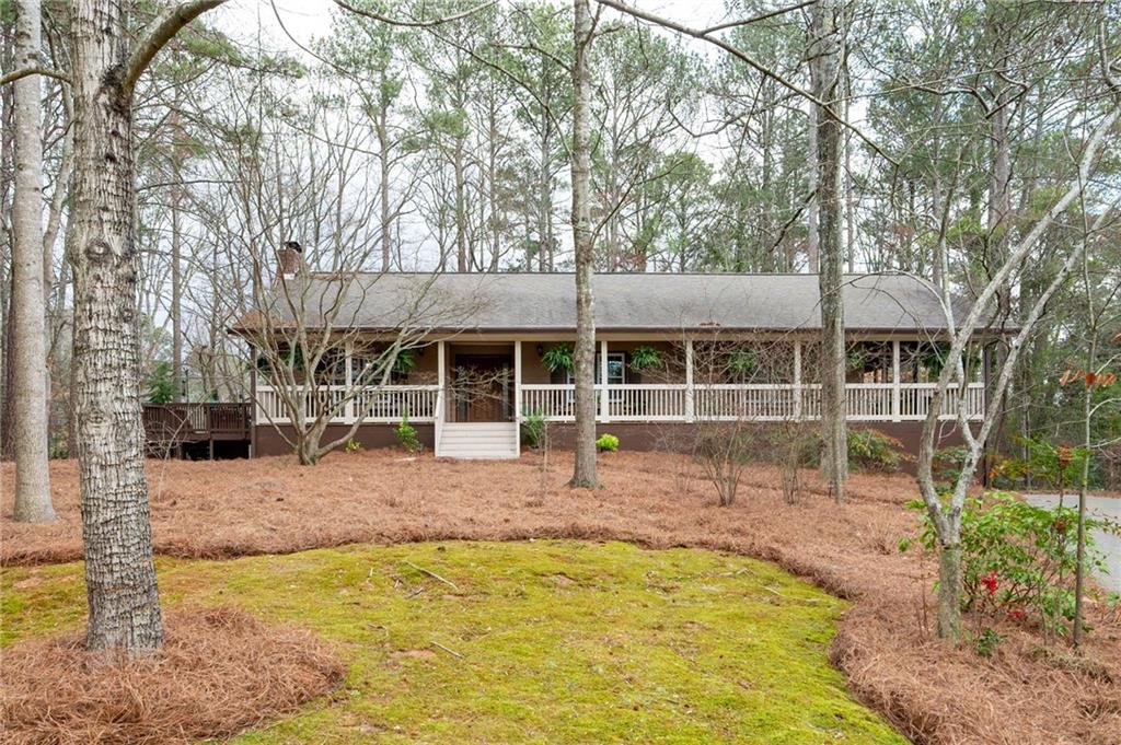 Single-story home with a long covered porch nestled among leafless trees.