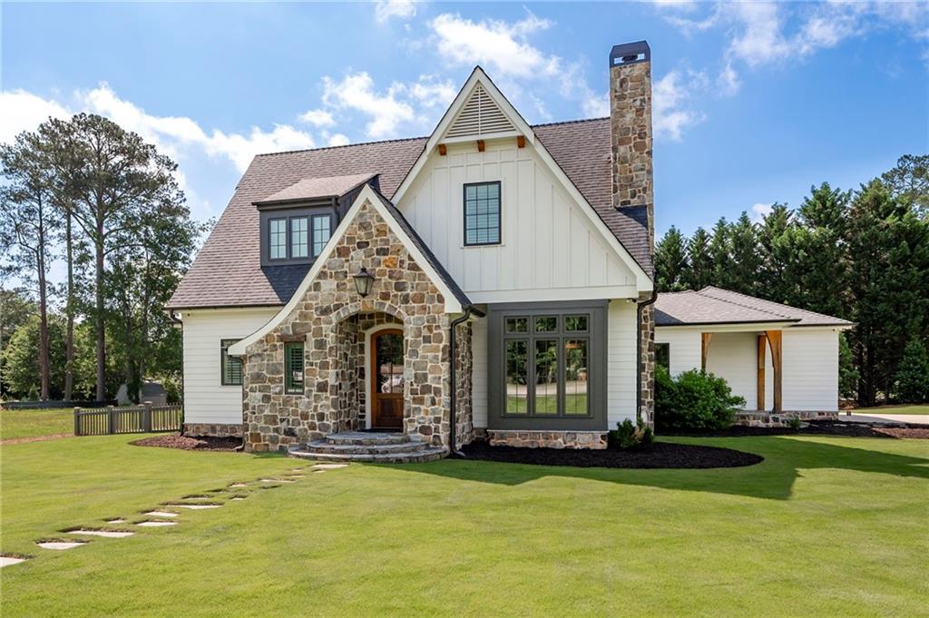White-and-stone home with steep gables, a tall stone chimney, and a broad green lawn.
